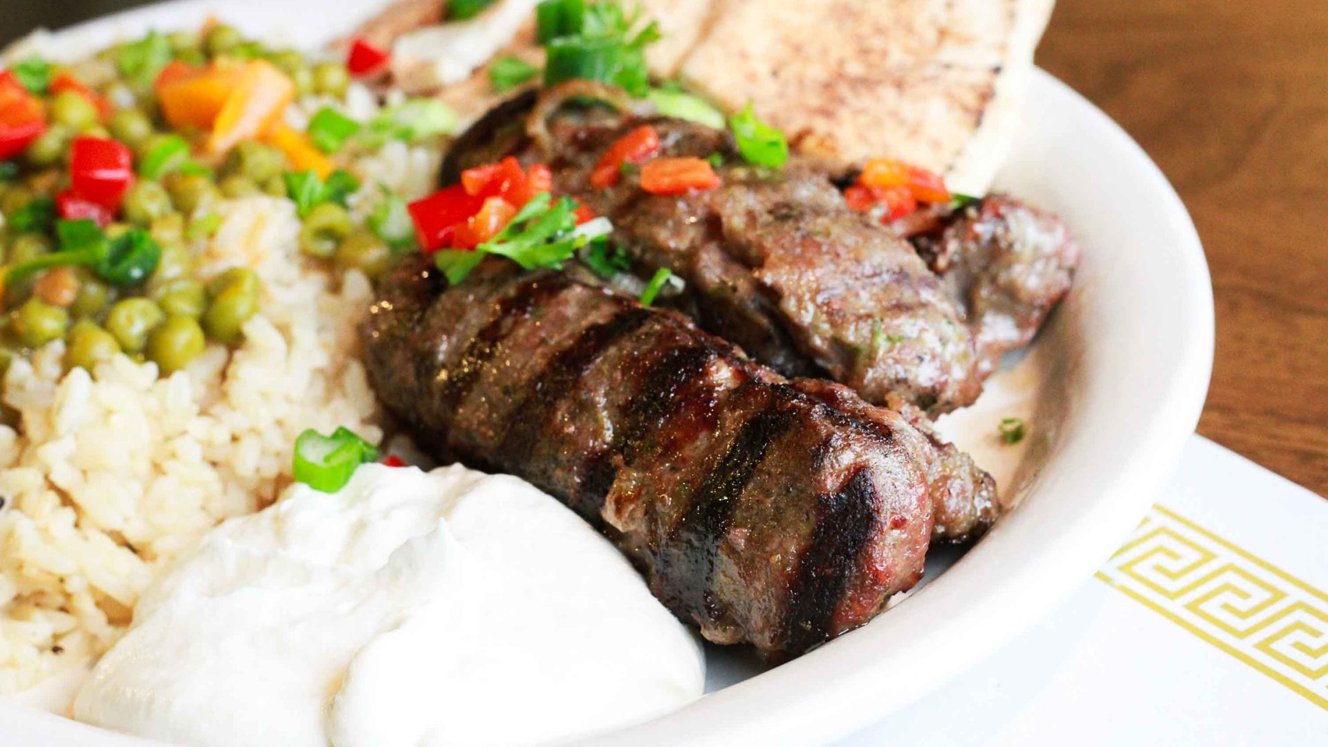 A plate of qofte with salad, bread and yoghurt.