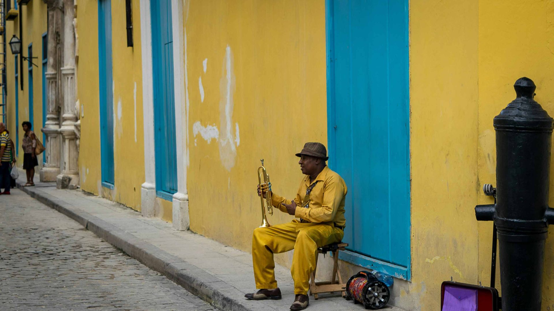 A man in yellow against a yellow building plays an instrument.