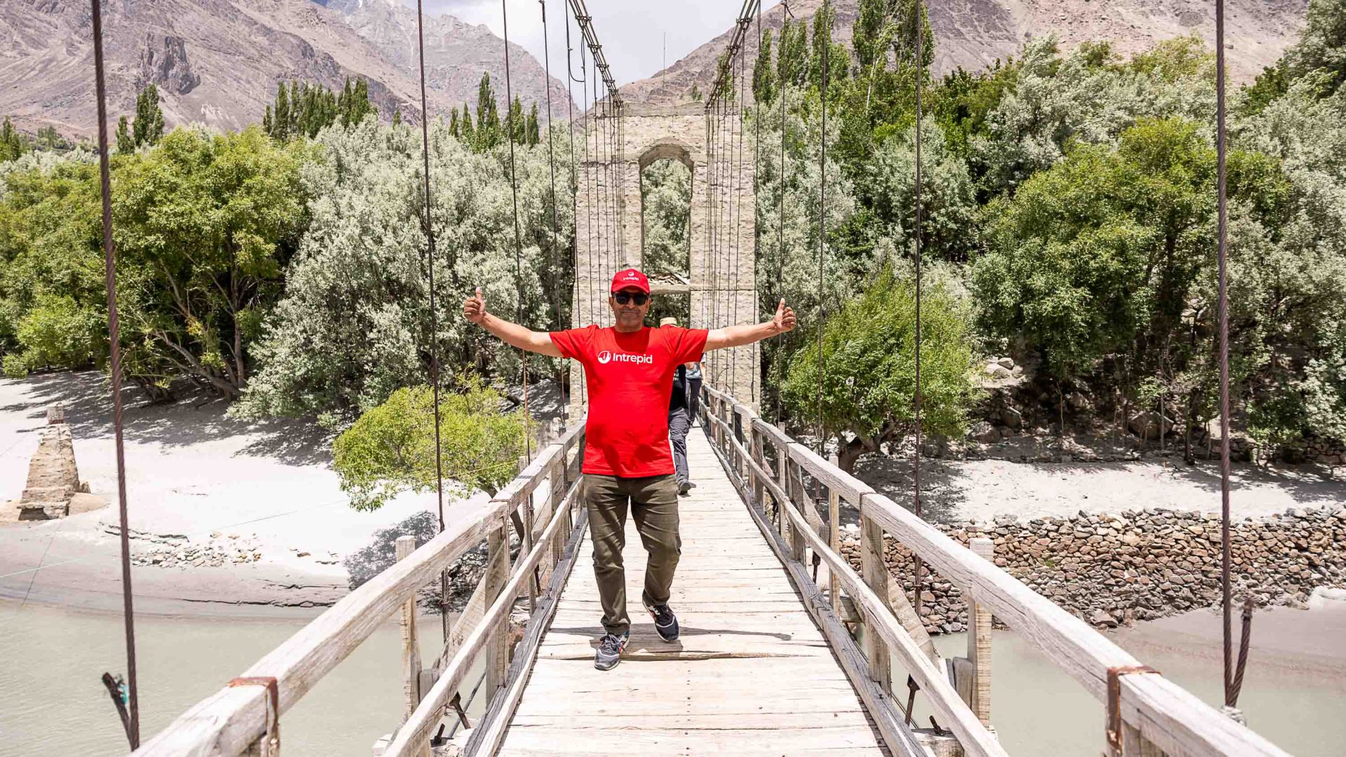 A man in red stands on a bridge with his arms outstretched.