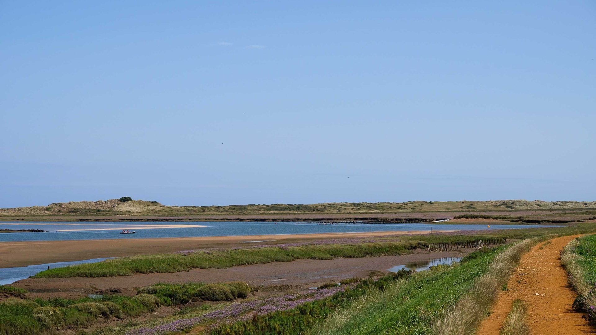 Blue water, dark sand and grassy paths.