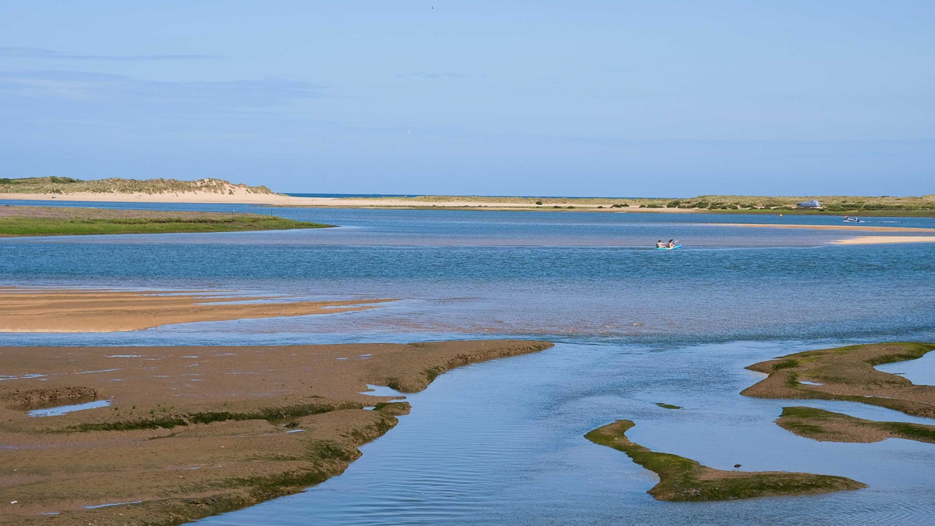 Blue water and dark sand in the foreground leads to white sand in the background.