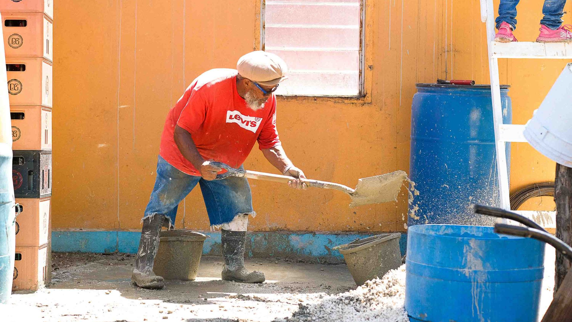 A man in a red t shirt shovels concrete at a house.