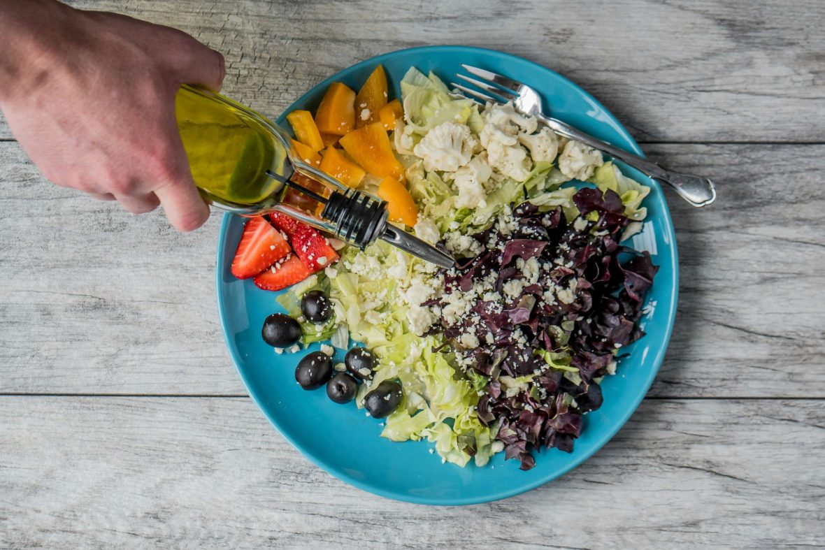 A colorful plate of salad with olive oil being poured on it.