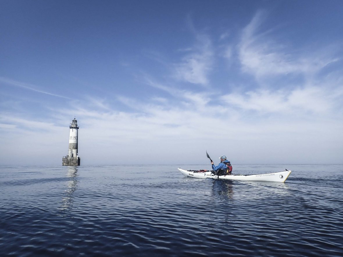 A man on a kayak with a lighthouse in the distance.