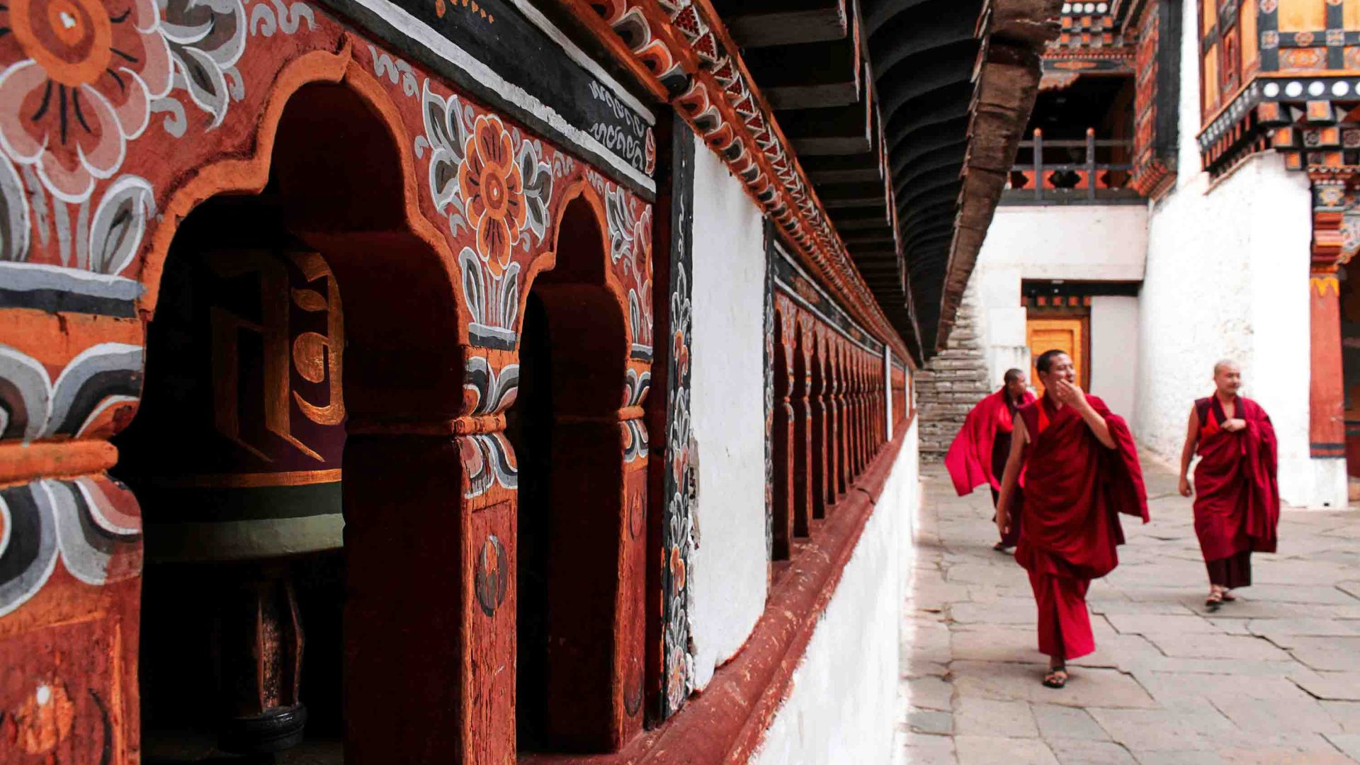 Monks at a temple, walking past prayer wheels.