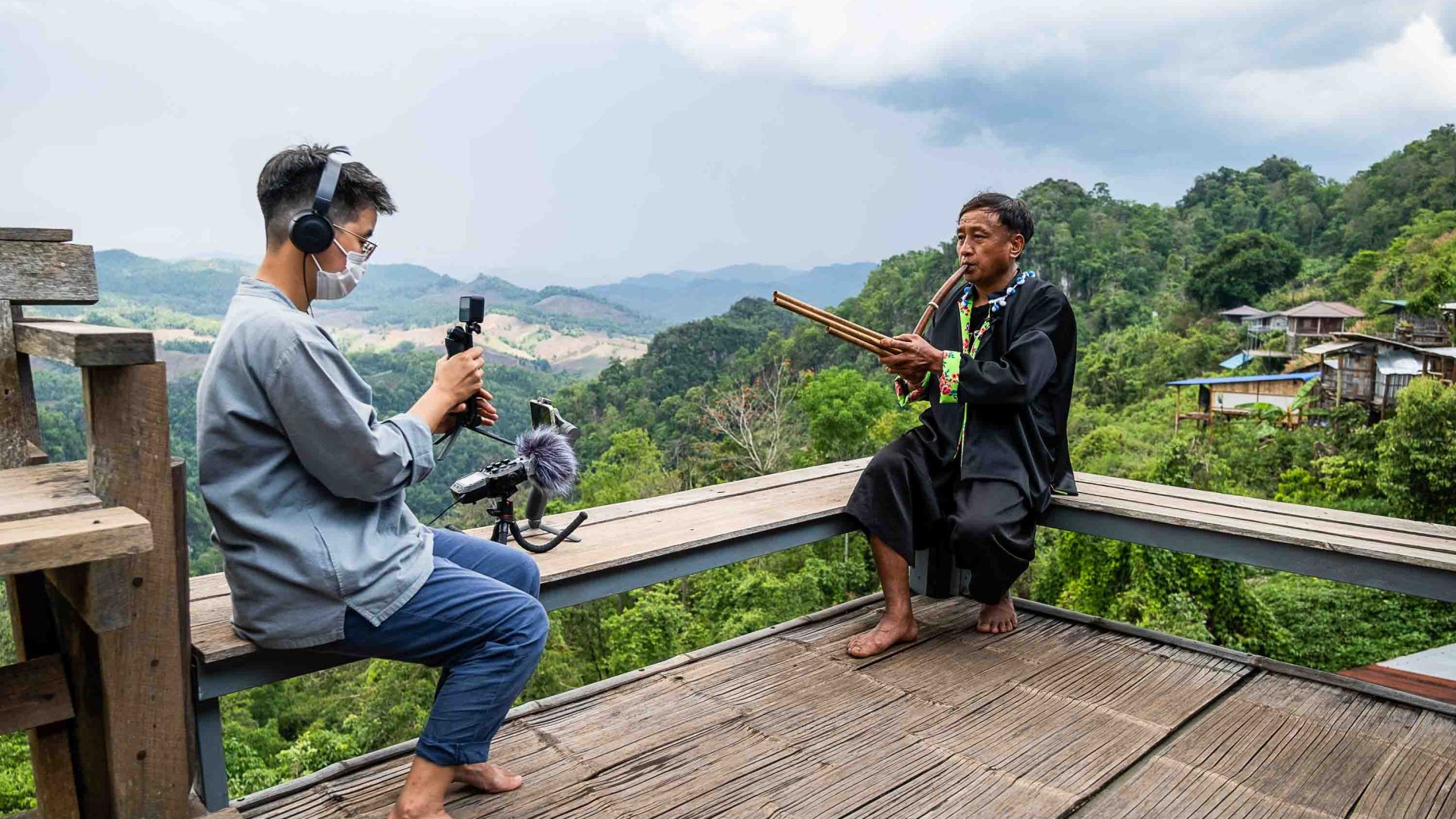 A woman records an Indigenous musician against a background of hills.