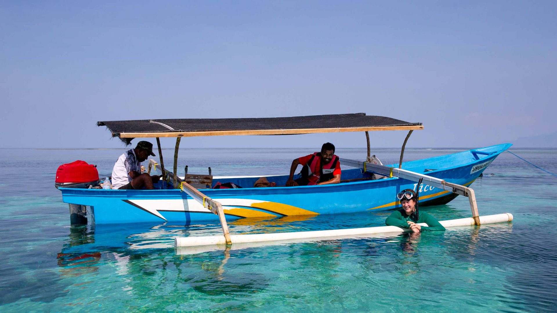 A traveler enjoys the pristine water off Arturo in Timor Leste. They hold the edge of a small boat.