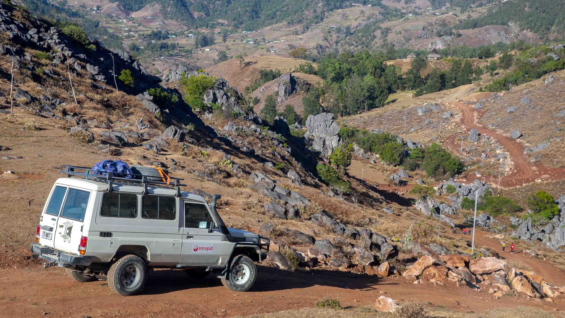 A jeep makes its way down a dusty and rocky road.