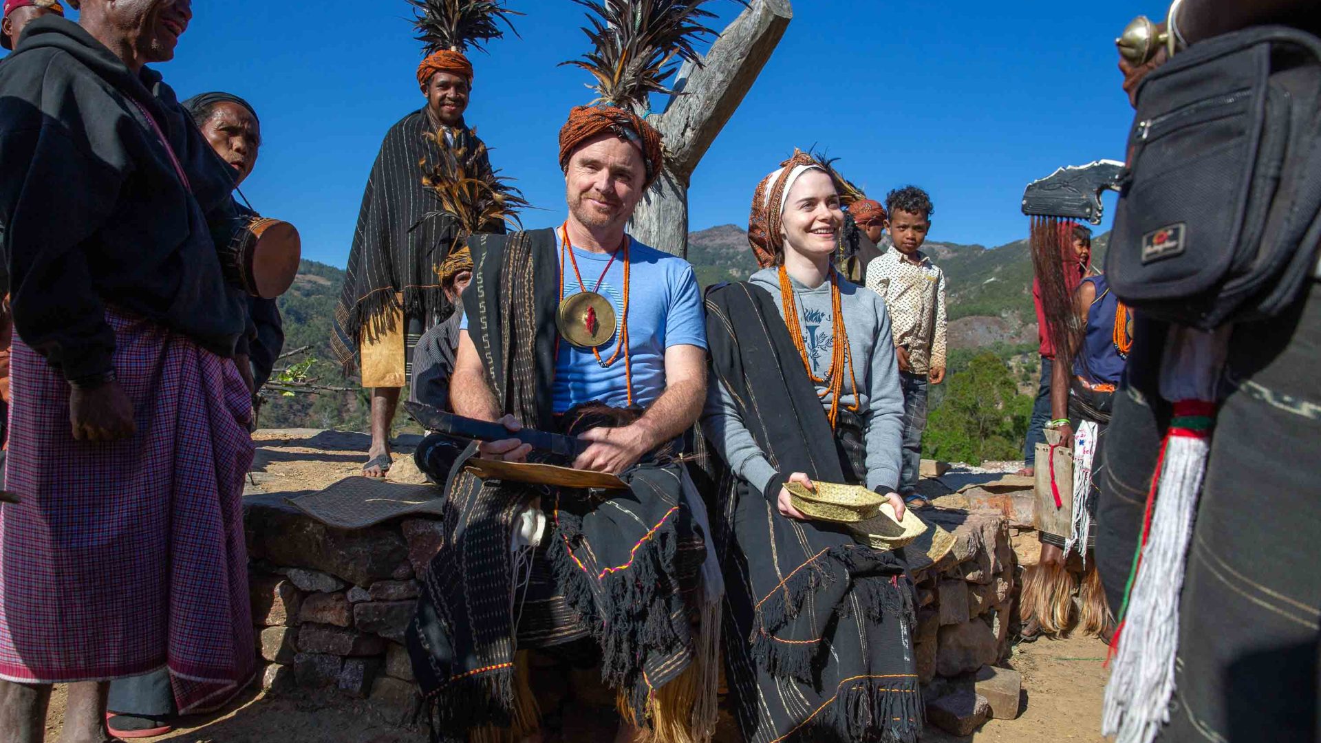 Travelers sit amongst a group of people participating in a welcome ceremony.