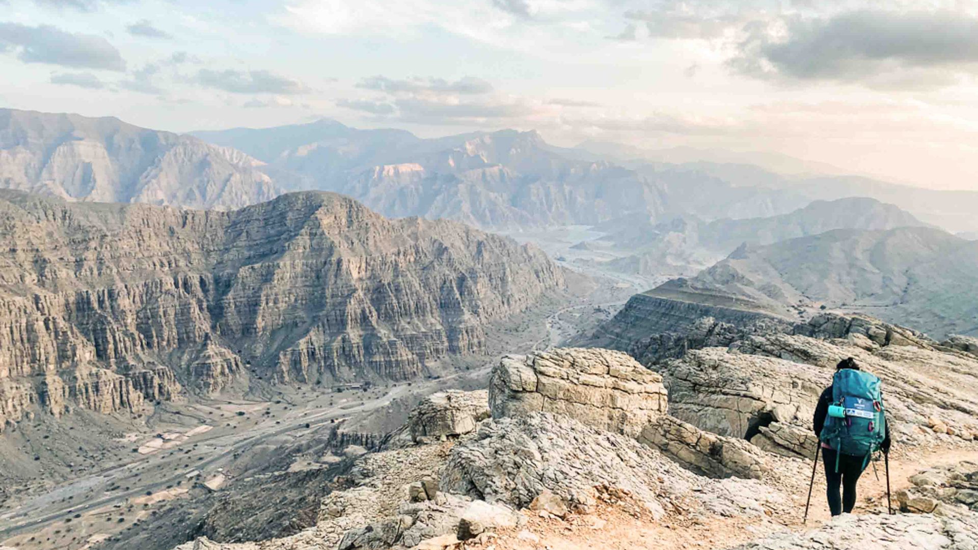 The back of a woman with a backpack overlooking a valley.